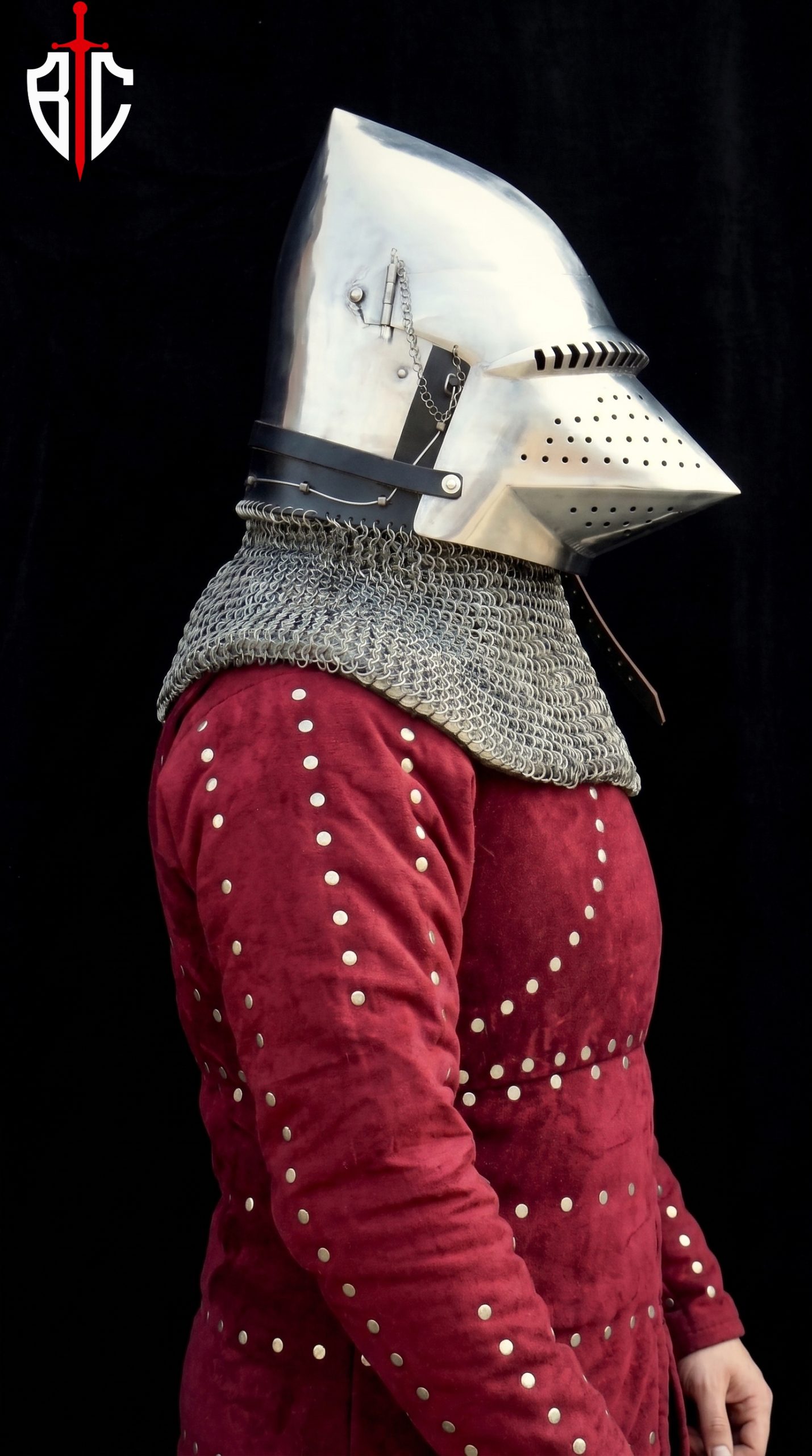 Pig face bascinet helmet front view with visor raised showing white quilted padded liner inside, riveted chainmail aventail covering neck, and pointed conical steel skull with chain stays